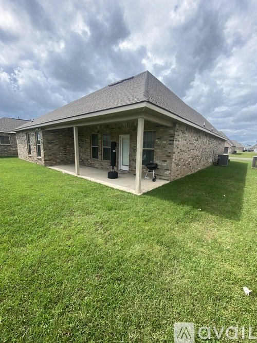 A house with a grey roof and a white door is surrounded by a grassy lawn.