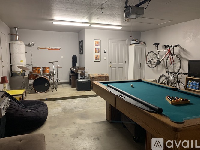 A room with a pool table, a bicycle, a drum set, and a TV.