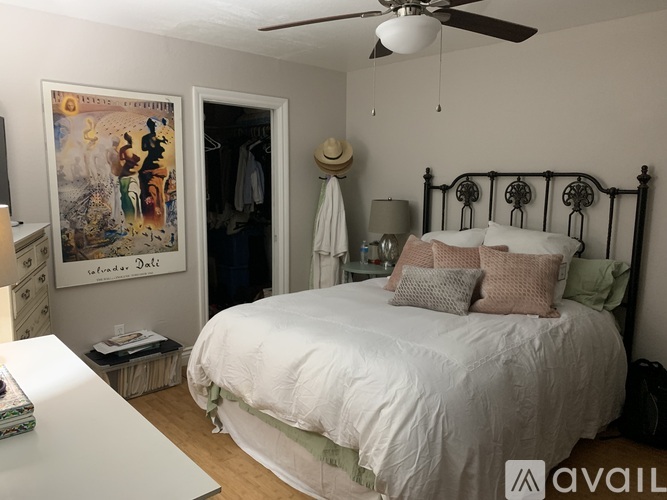 A bedroom with a bed, a ceiling fan, and a painting on the wall.
