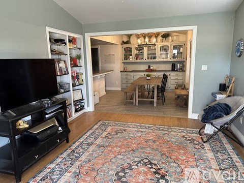 A living room with a rug on the floor and a television on the left.