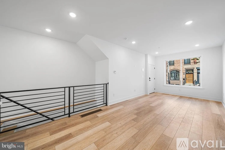 A spacious room with wooden flooring and a balcony with a metal railing.
