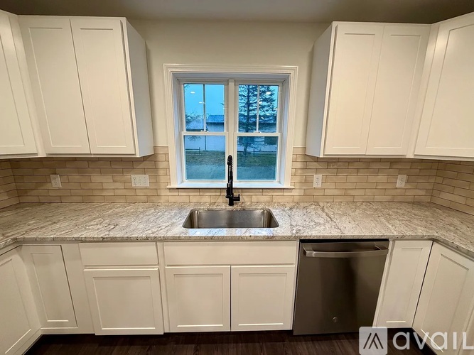 A kitchen with white cabinets and a window overlooking a snowy landscape.