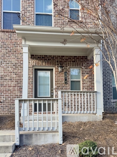 A brick house with a porch and a tree in front.