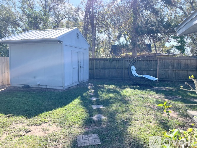 A small white shed sits in a backyard with a wooden fence and a blue tarp on the ground.