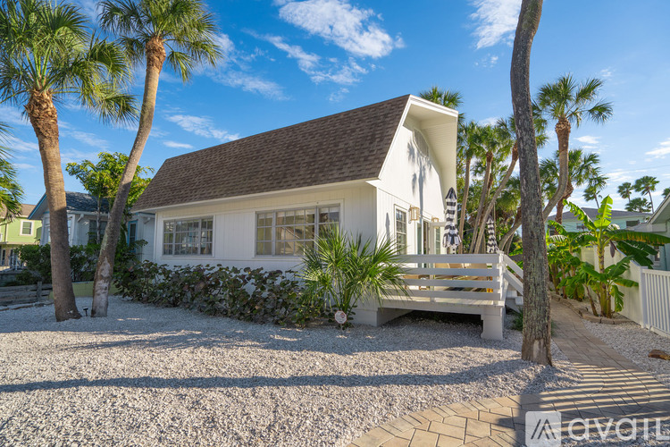 A white house with a brown roof is surrounded by palm trees.