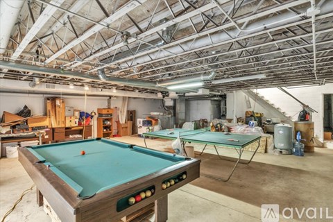 A pool table in a room with a high ceiling and exposed pipes.