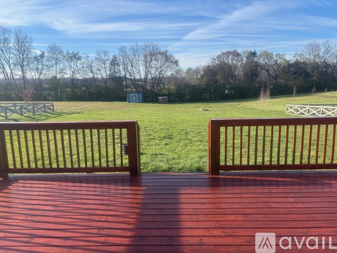 A wooden deck with a bench overlooking a green field.
