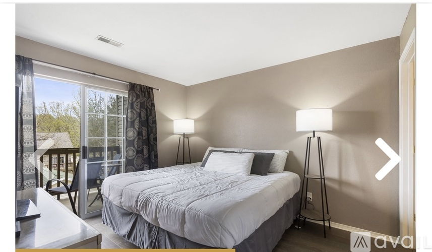 A bedroom with a large bed and a balcony with a view of trees.