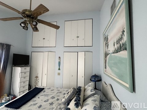 A bedroom with a bed, a ceiling fan, and a painting on the wall.