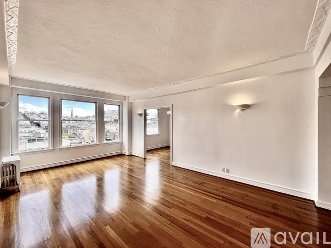 A room with wooden floors and white walls, with a window showing a cityscape outside.