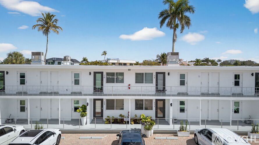 A white building with a balcony and a palm tree in the background.