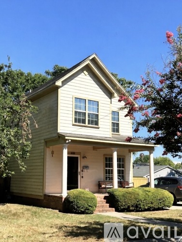 A small house with a front porch and a tree with red flowers to the right.