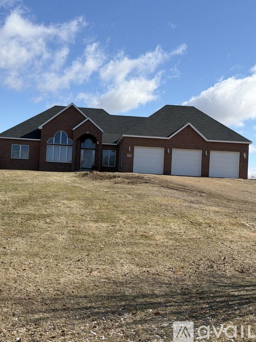 A house with a brown roof and white windows is surrounded by a grassy field.