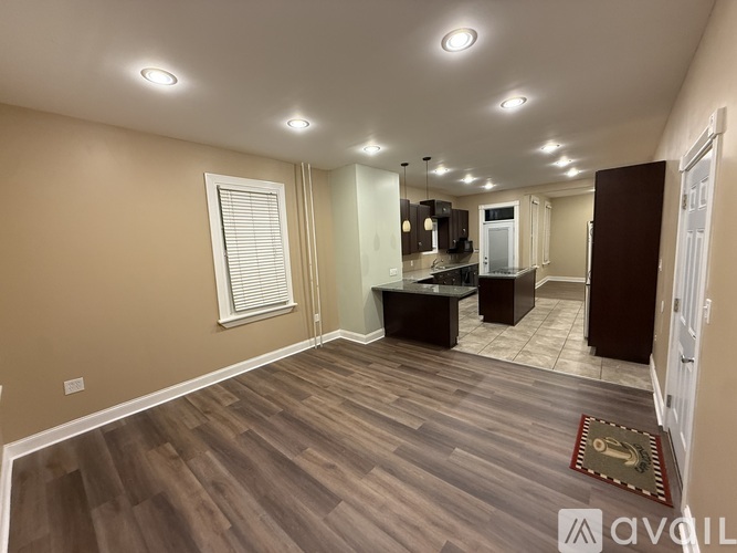 A spacious room with wooden flooring and a kitchen area in the background.