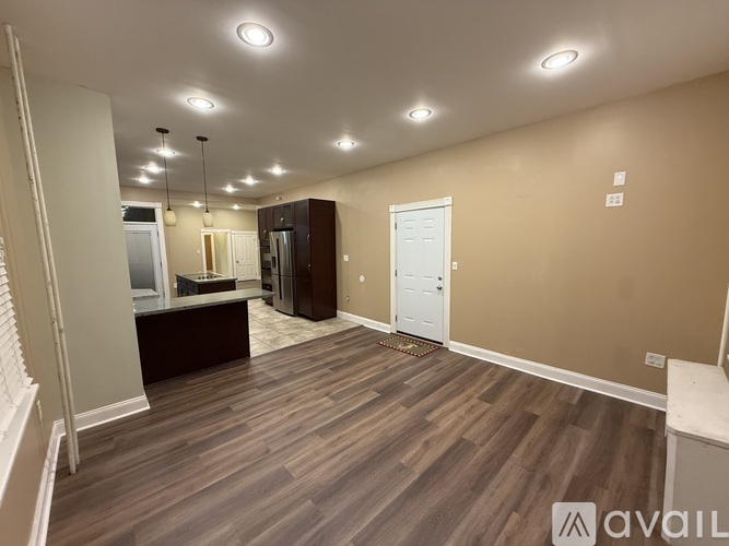 A spacious room with wooden flooring and a kitchen area with appliances.