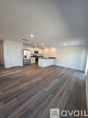A room with wooden flooring and a kitchen area in the background.