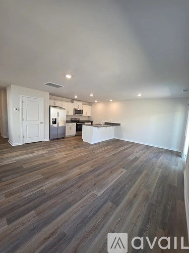 A room with wooden flooring and a kitchen area in the background.