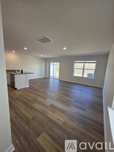 A spacious room with wooden flooring and a kitchen area to the left.