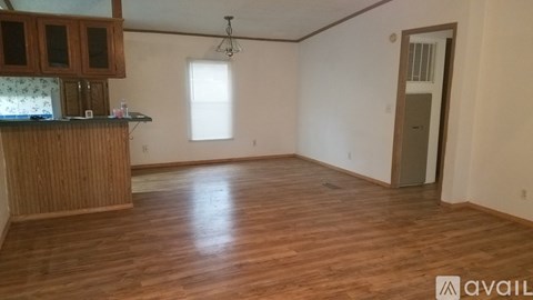 A room with wooden flooring and a kitchen area with cabinets and a window.