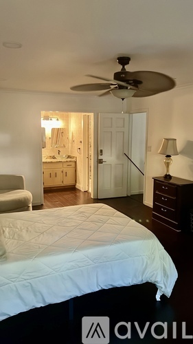 A bed with a grey comforter and two black pillows sits in a room with a painting on the wall and two lamps on either side of the bed.