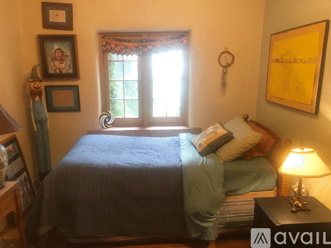 A bedroom with a bed, nightstand, lamp, and pictures on the wall.