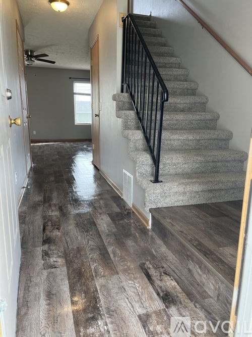 A hallway with a staircase and wood flooring.
