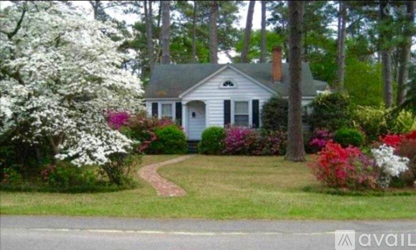 A white house with a grey roof surrounded by green trees and bushes.