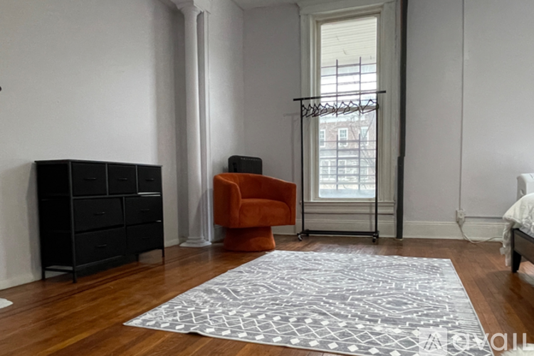 A room with a black dresser, an orange chair, and a large rug.