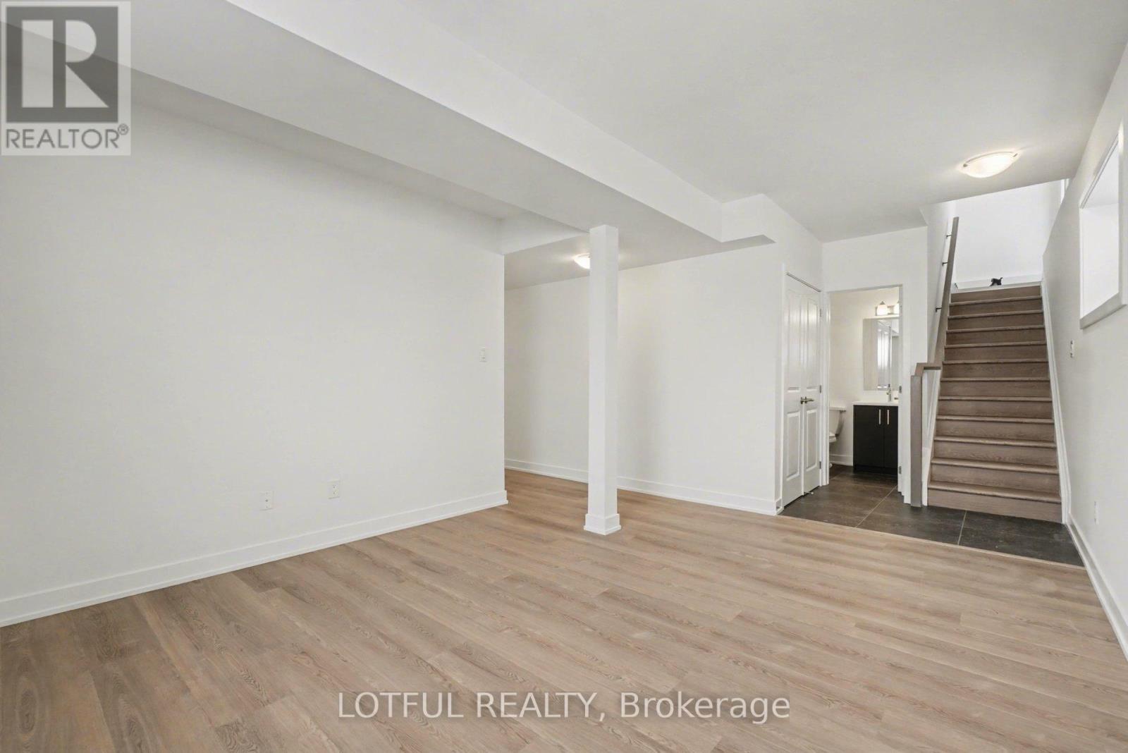 A spacious room with wooden flooring and white walls, with a staircase leading to another level.