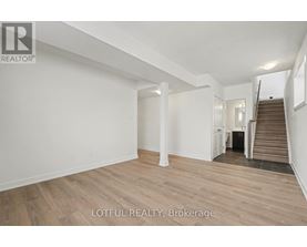 A spacious room with wooden flooring and white walls, with a staircase leading to another level.