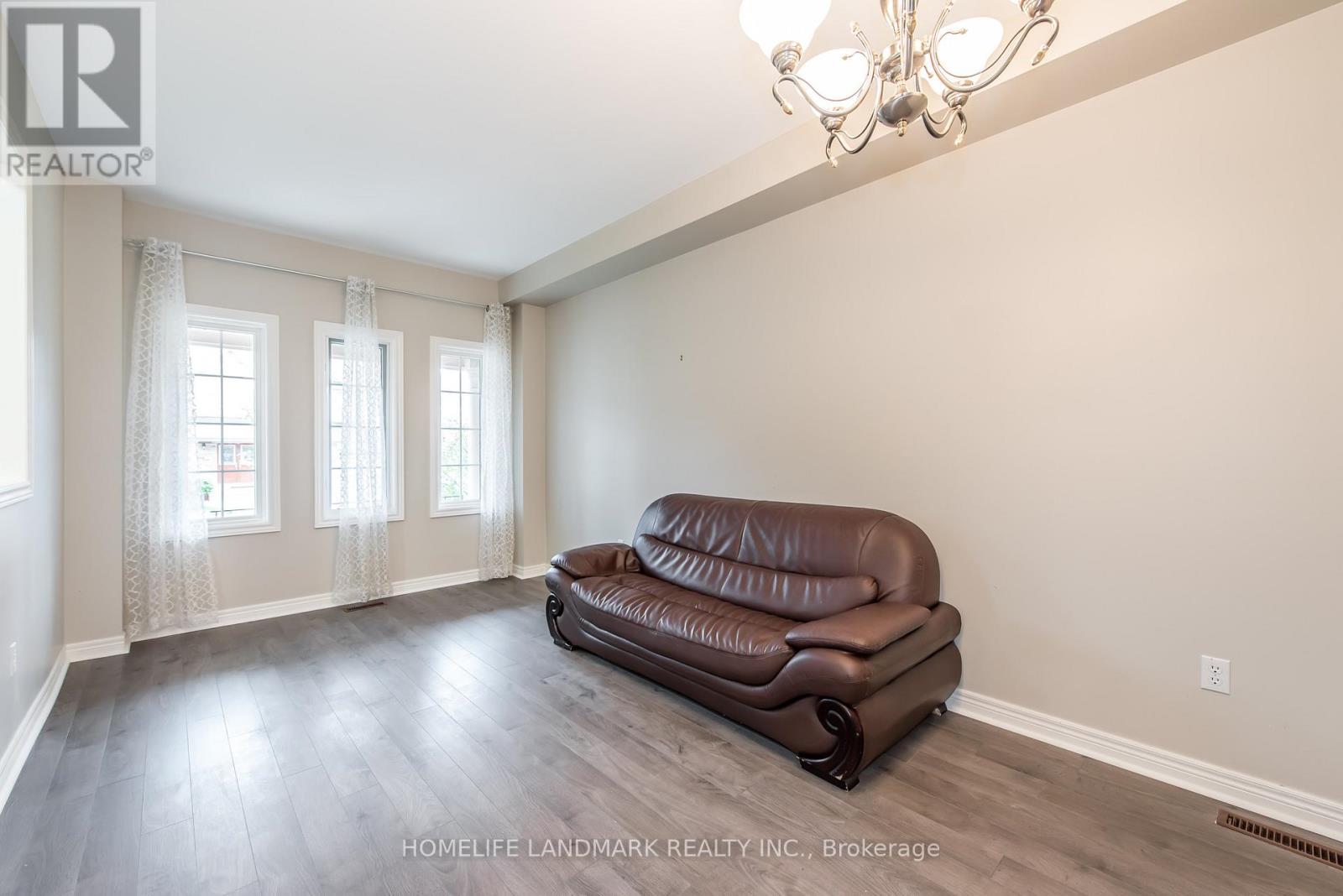 A brown leather sofa sits in a room with wooden floors and a chandelier.
