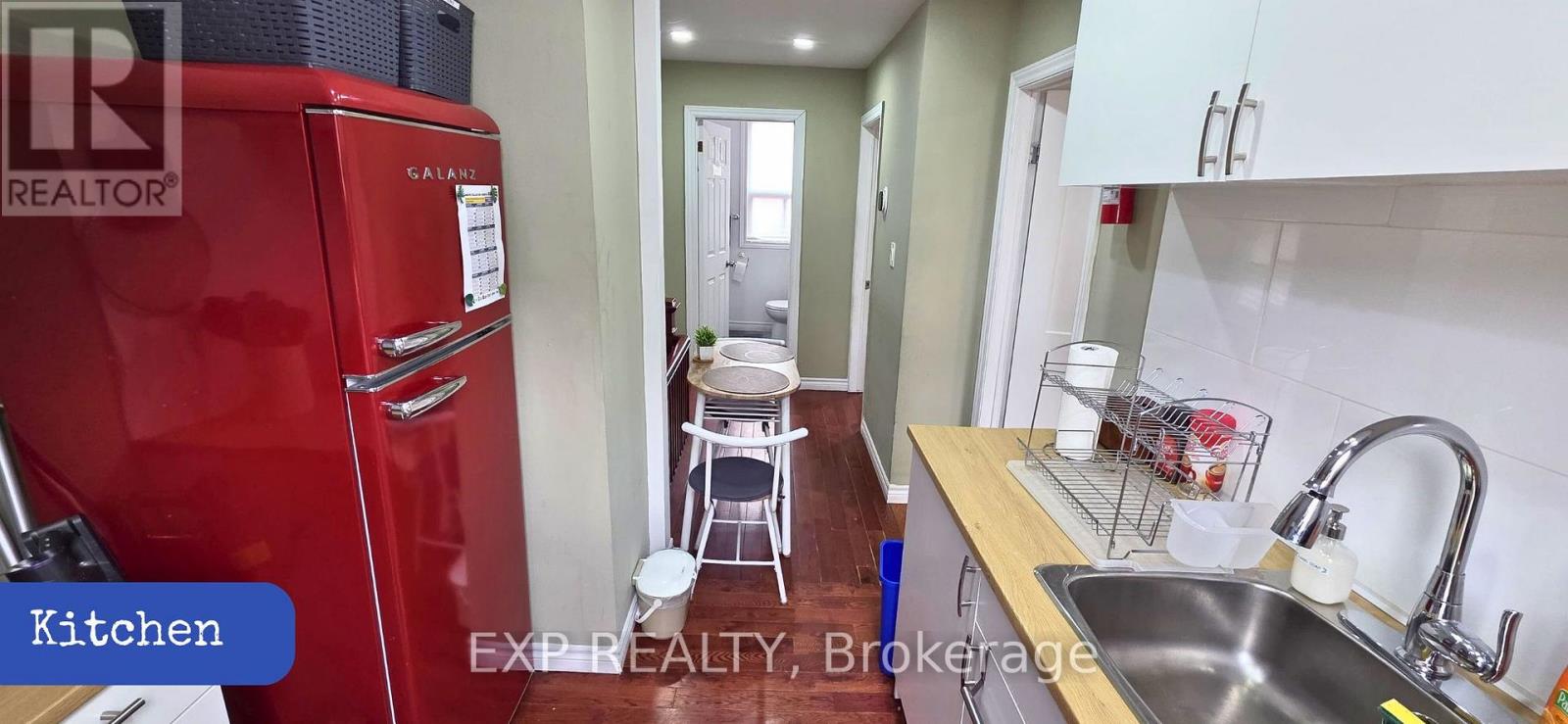 A red fridge in a kitchen with a sink and a dish rack.