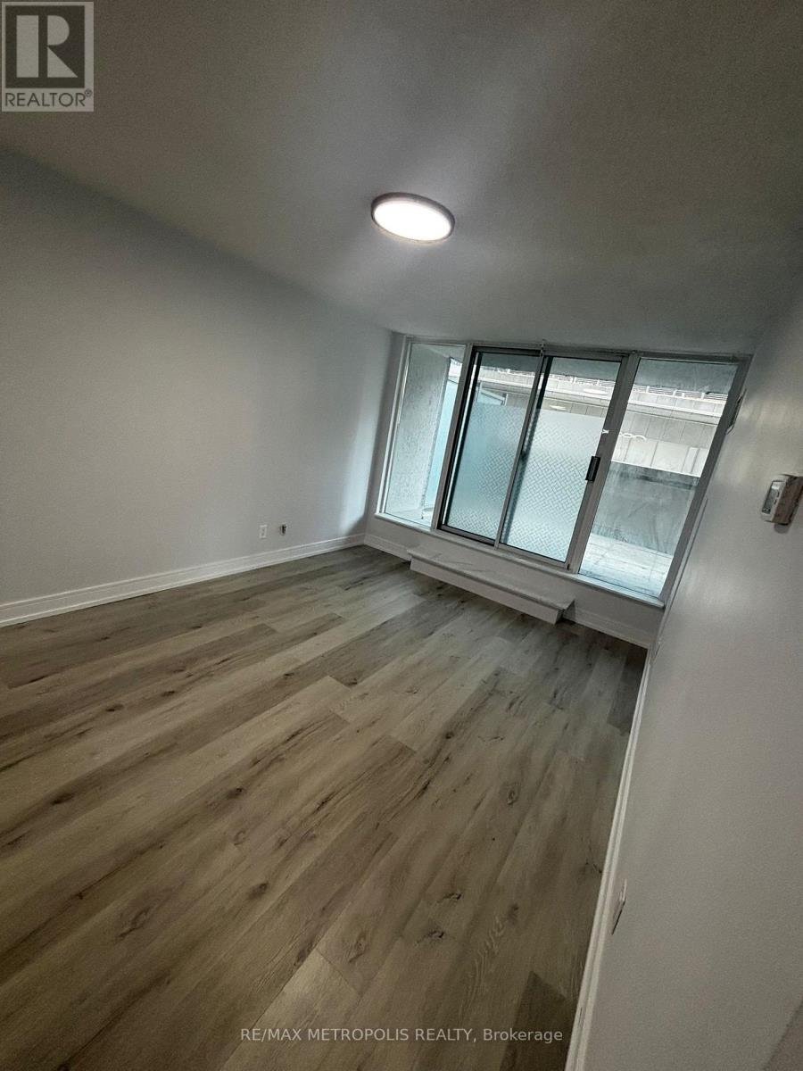 A room with wooden flooring and a window with a view of a building outside.