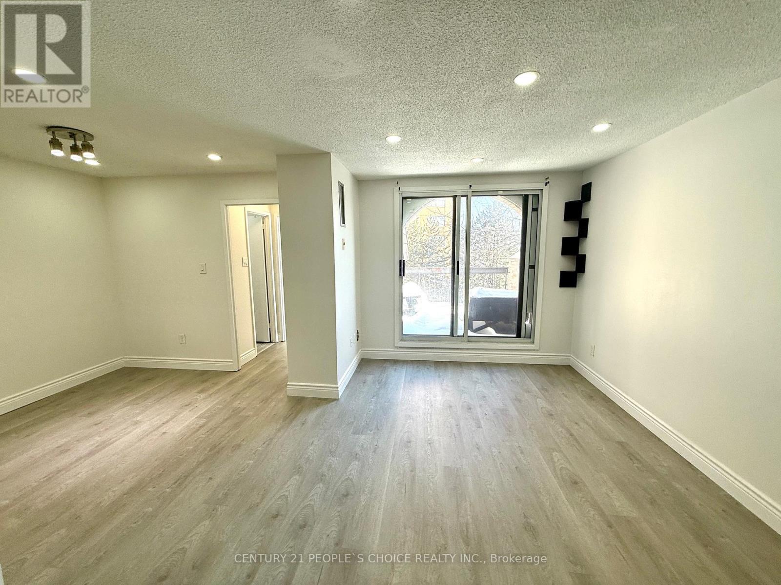 A spacious room with light wood flooring and a sliding glass door leading to a balcony.