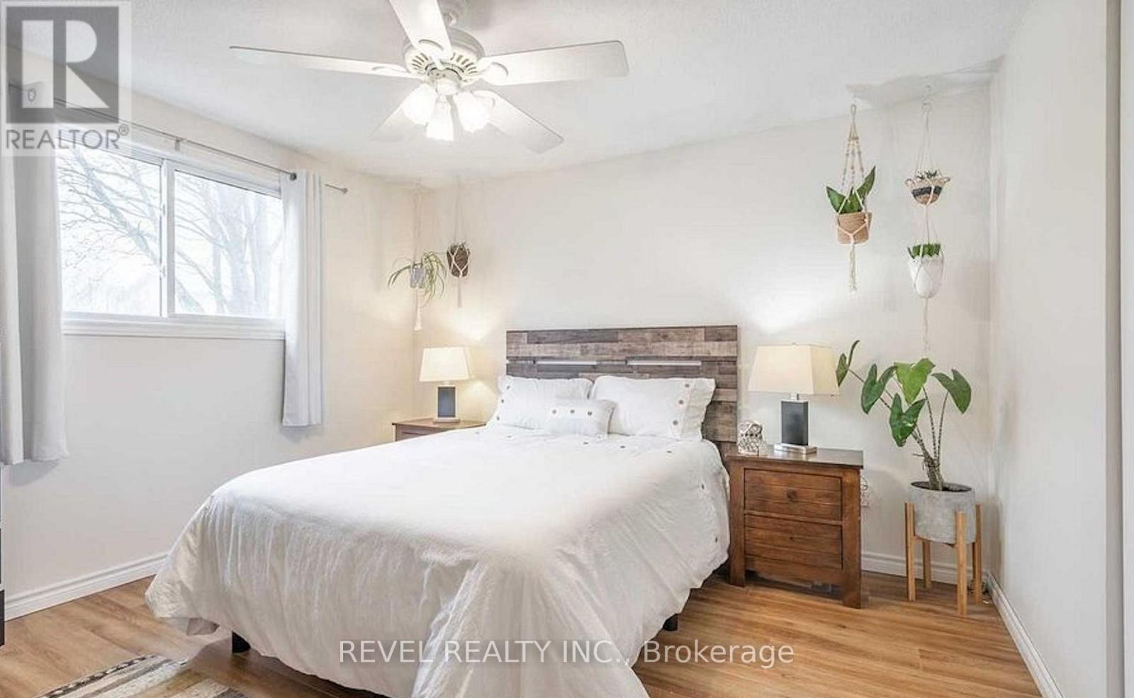 A bedroom with a white bed, wooden nightstand, and a ceiling fan.