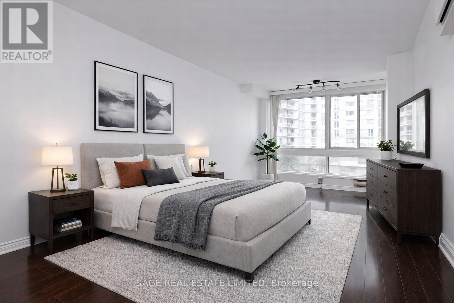 A bedroom with a large bed, a nightstand with a lamp, and a framed picture on the wall.