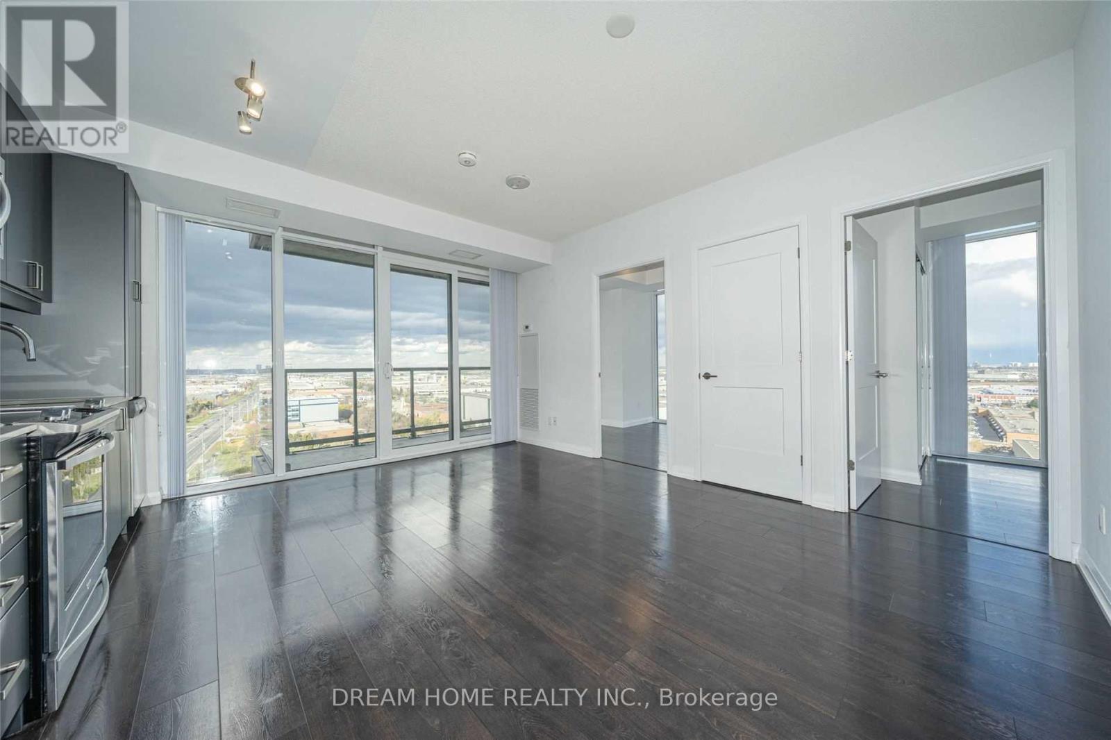 A spacious, empty room with wood floors and large windows overlooking a cityscape.