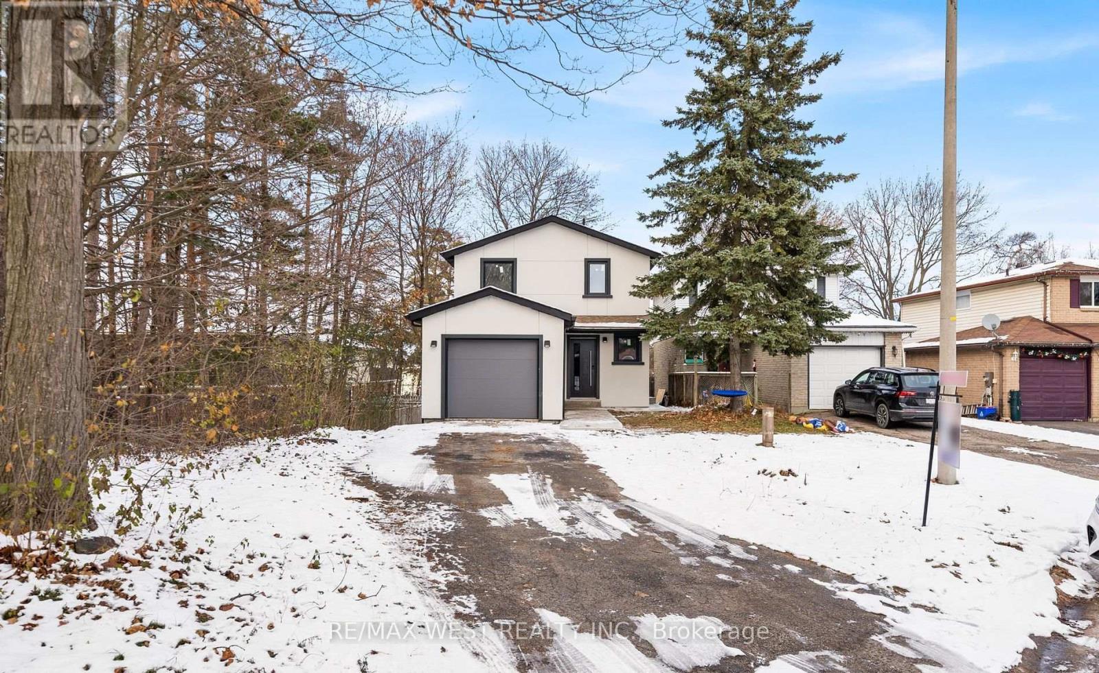 A house with a garage is surrounded by snow and trees.