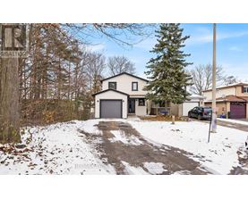 A house with a garage is surrounded by snow and trees.