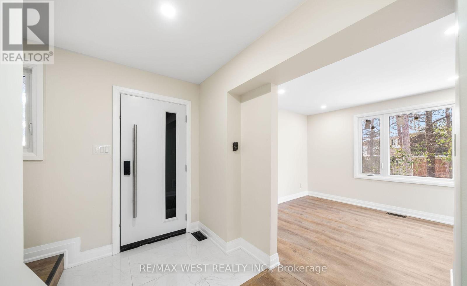 A room with a white door and a window with a view of trees outside.