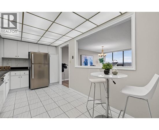 A kitchen area with a refrigerator, a dining table with two chairs, and a window with a view of the outdoors.
