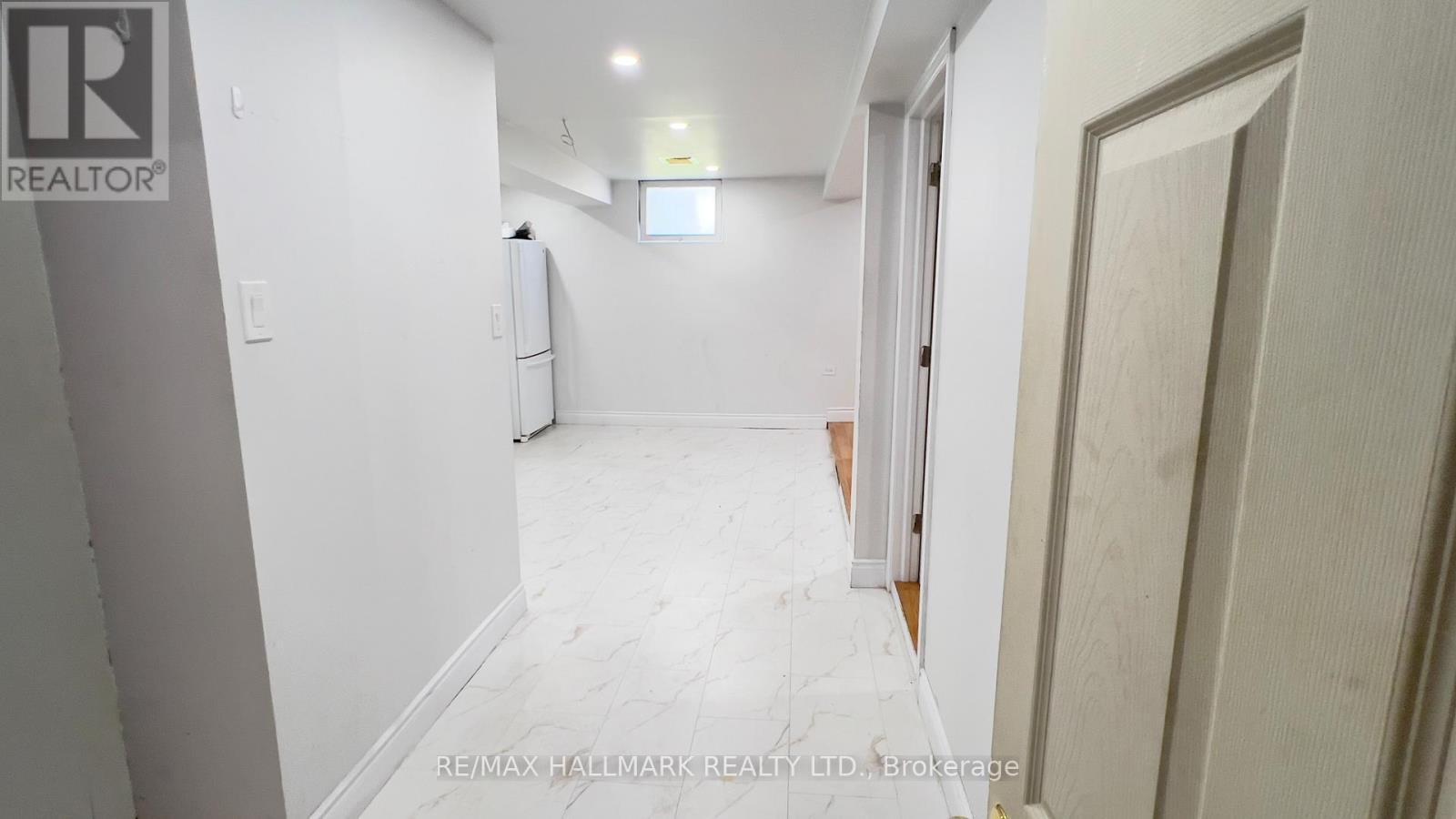 A white hallway with a door on the right and a window in the middle of the wall.