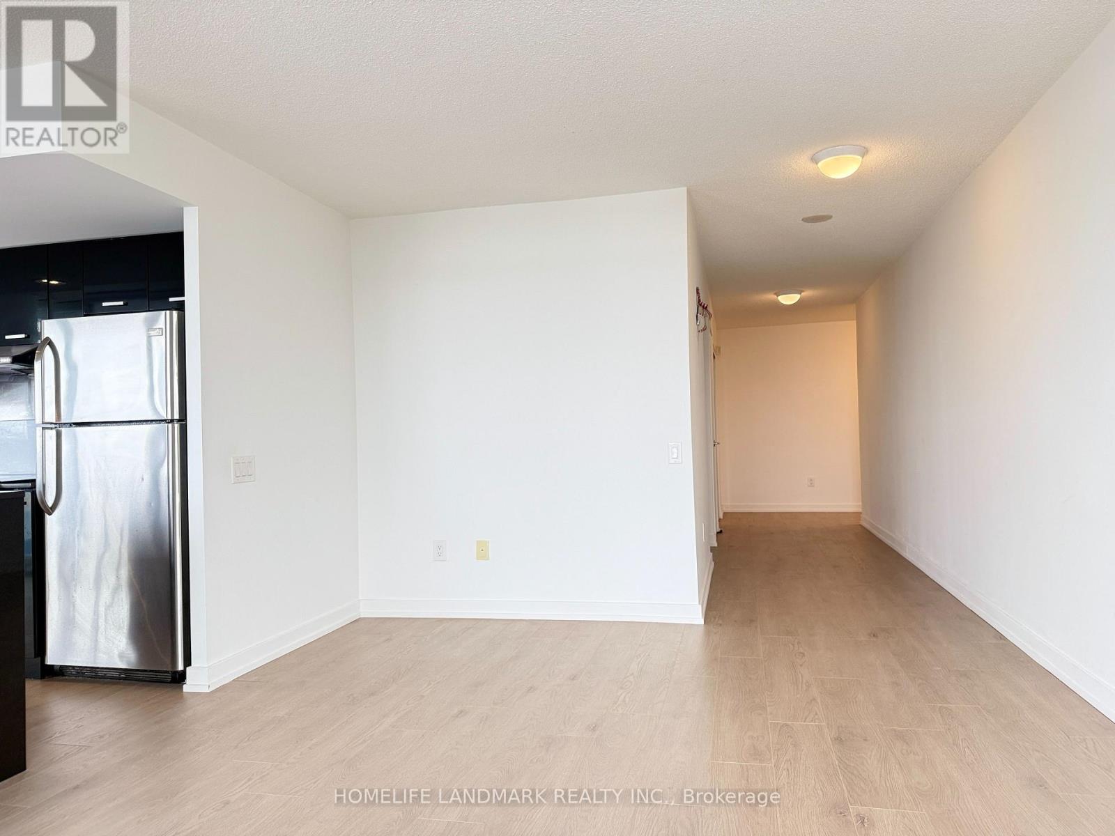 A spacious, empty room with a refrigerator on the left side.