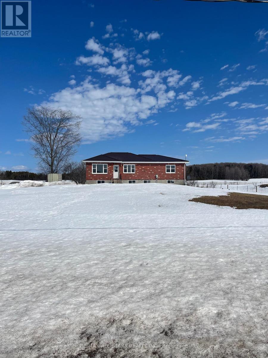 A red brick house with a white door and windows is surrounded by a snowy field.