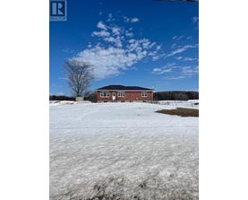 A red brick house with a white door and windows is surrounded by a snowy field.