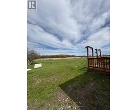 A wooden deck overlooks a grassy field with a cloudy sky above.