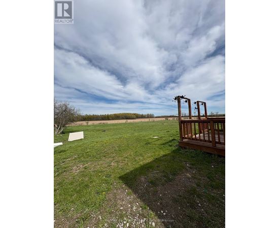 A wooden deck overlooks a grassy field with a cloudy sky above.