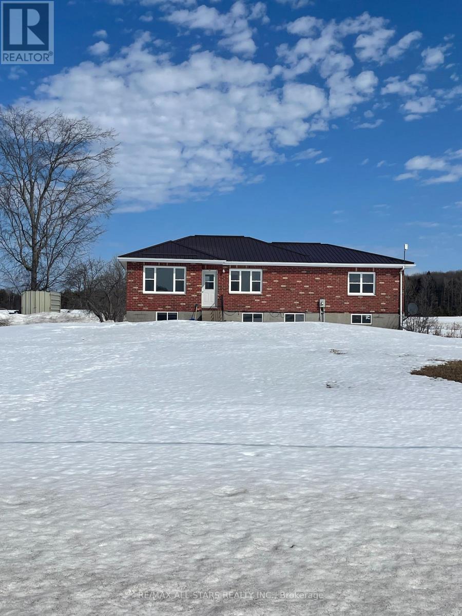 A house with a black roof and red brick walls sits in a snowy field.