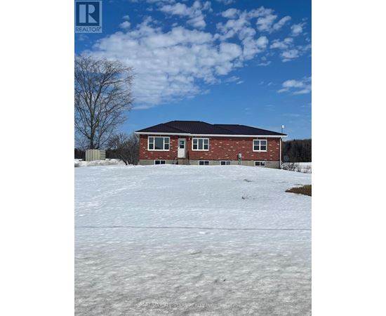 A house with a black roof and red brick walls sits in a snowy field.
