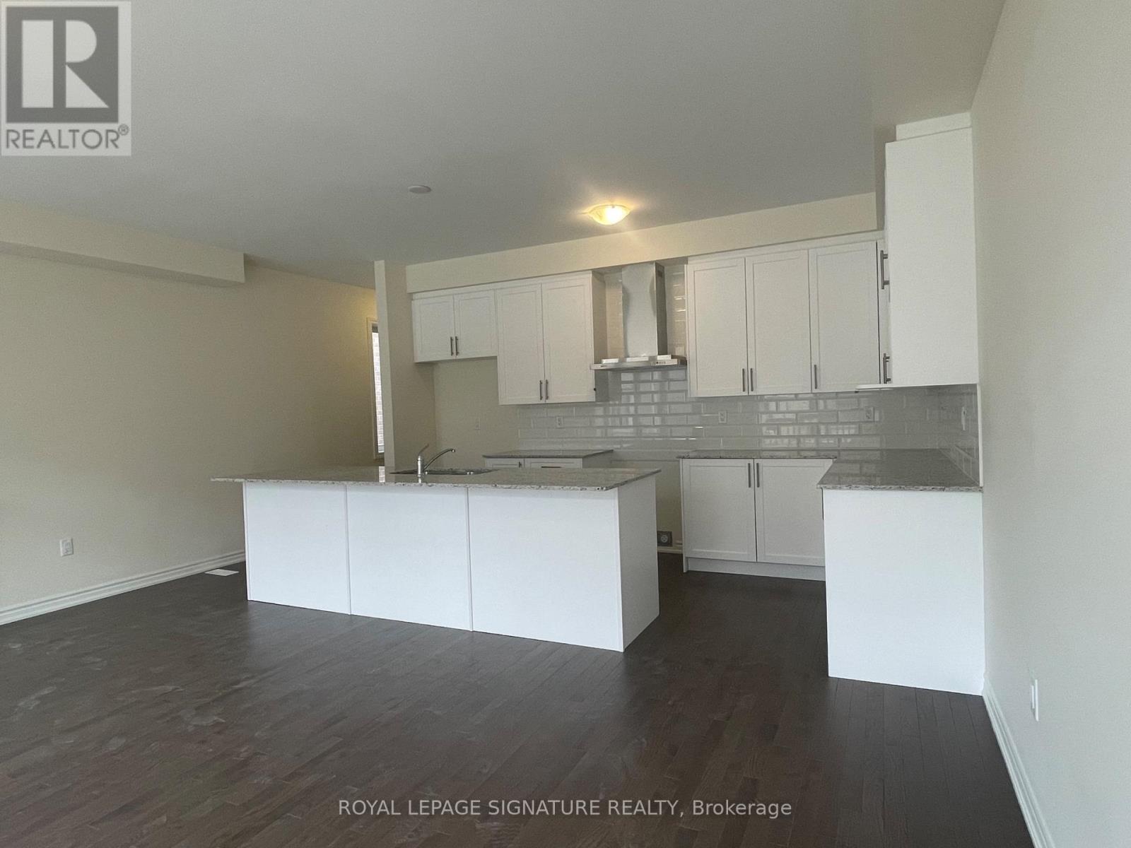 A spacious kitchen with white cabinets and a grey backsplash.
